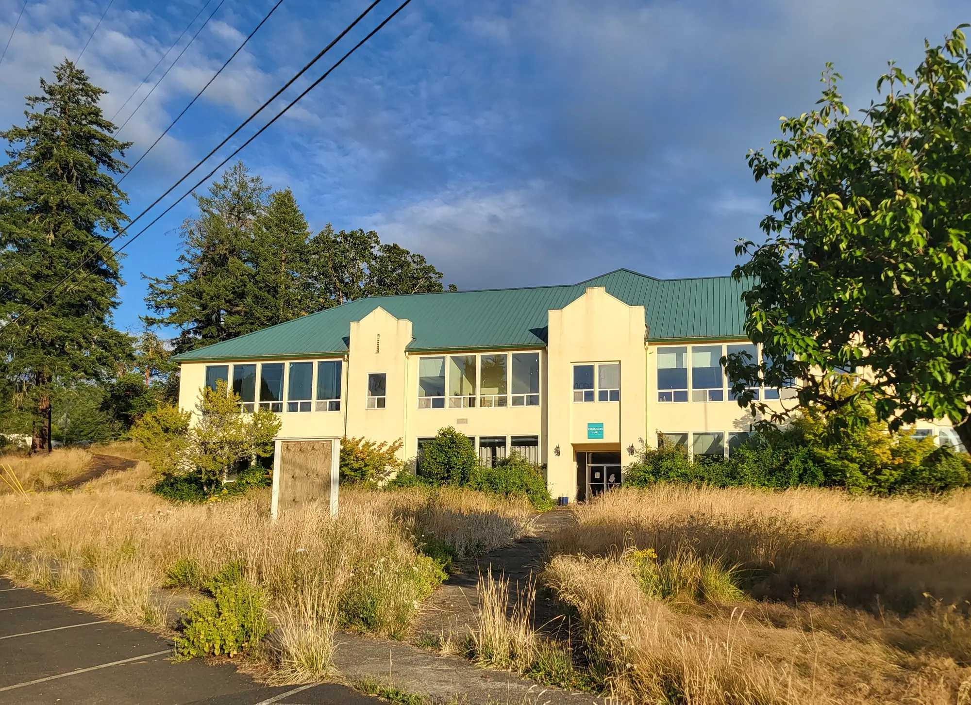 Current condition of the main building on the proposed GG's House campus, with tall grass and an empty parking area